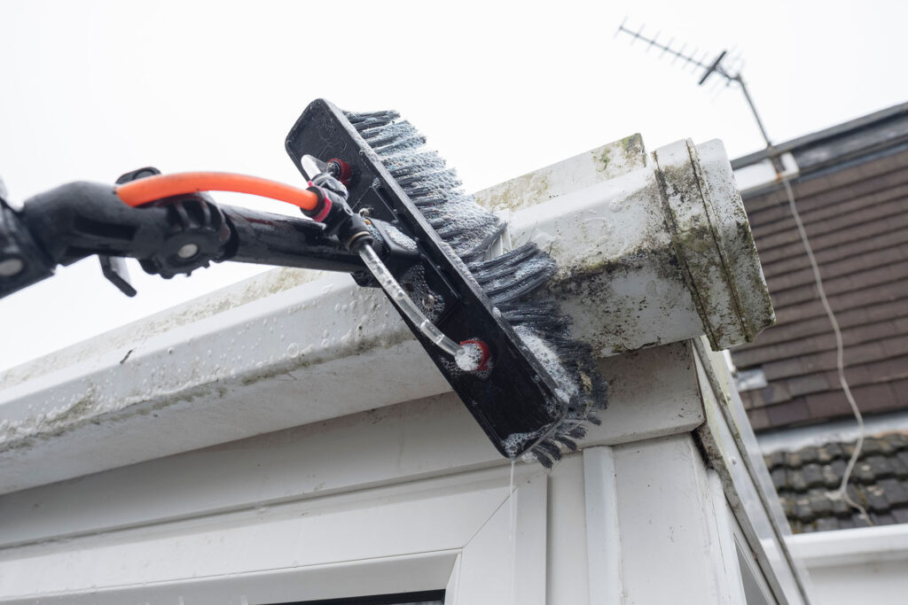 A cleaning professional in Leighton Buzzard meticulously cleaning gutter, fascia, soffit, and UPVC on a residential building.